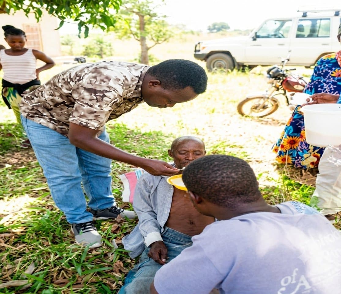 A UPSDE volunteer gently feeding an elderly community member during an outreach visit